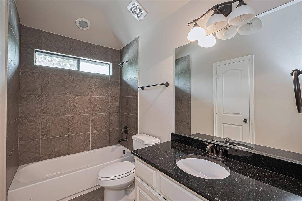 En-suite bathroom with granite countertop, tub/shower combo with tile surround, tile flooring and transom window.