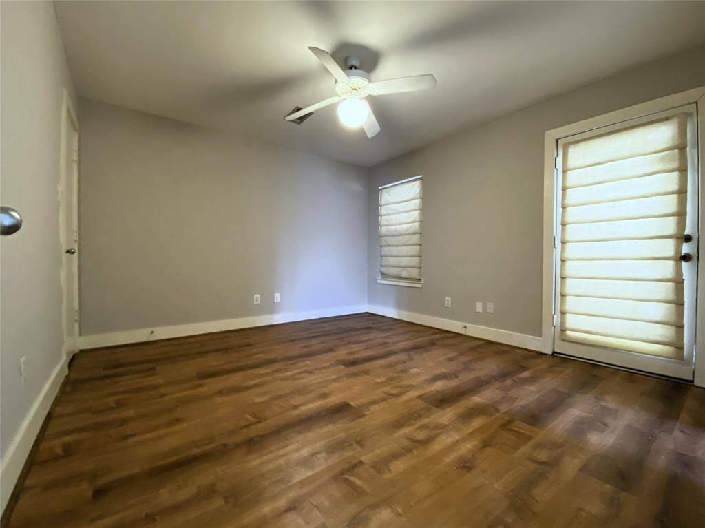 The 1st floor bedroom offers a ceiling fan with light fixture. Beyond a glass paned door is a patio.