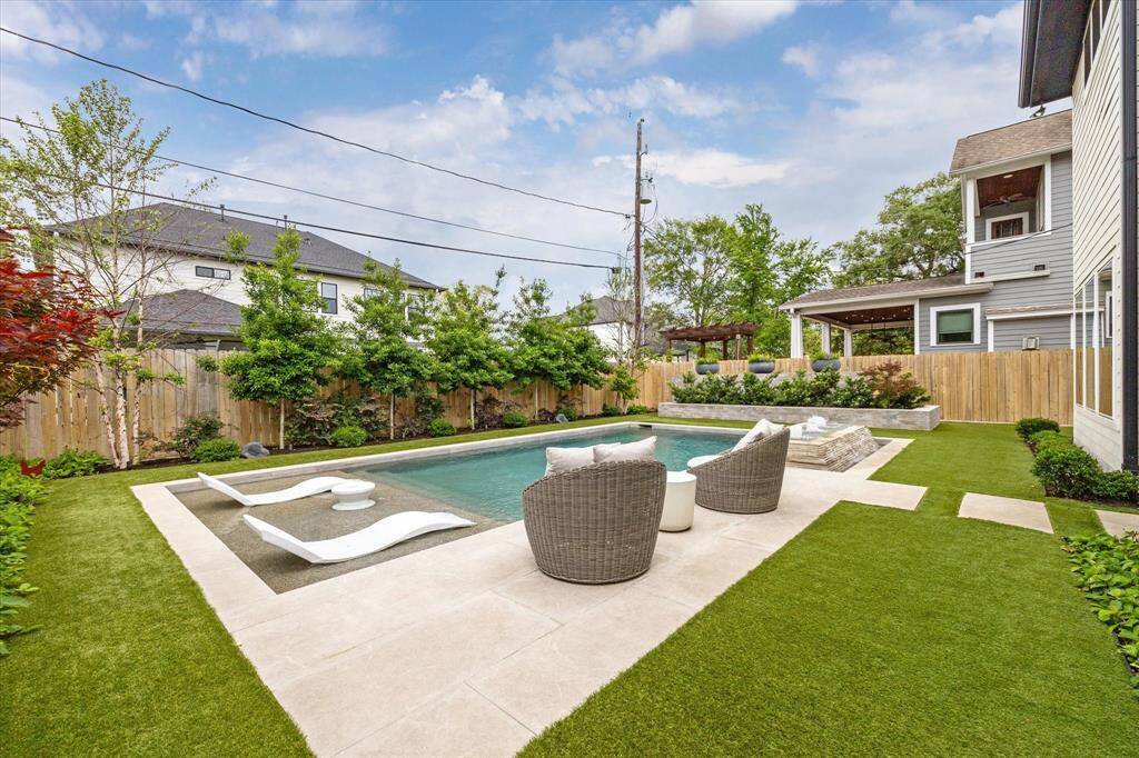 The pool deck showcases travertine tile and turf is laid along the perimeter of the pool deck.