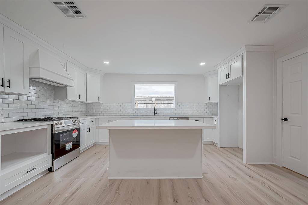 Timeless designer kitchen pairs wall-to-wall shaker cabinetry and a classic subway-tile backsplash with an oversized quartz island, picture-window sink, and dedicated fridge alcove—blending everyday function with clean modern style.