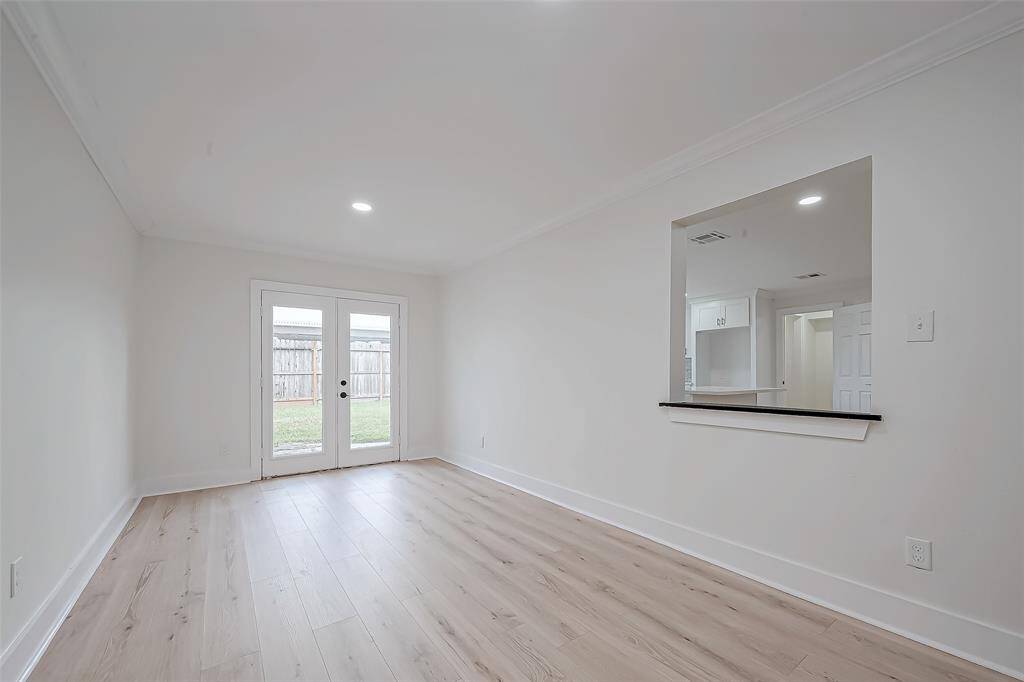 Airy flex room shines with light wood floors and fresh white walls, framed by glass French doors opening to the backyard and a handy kitchen pass-through for seamless entertaining.