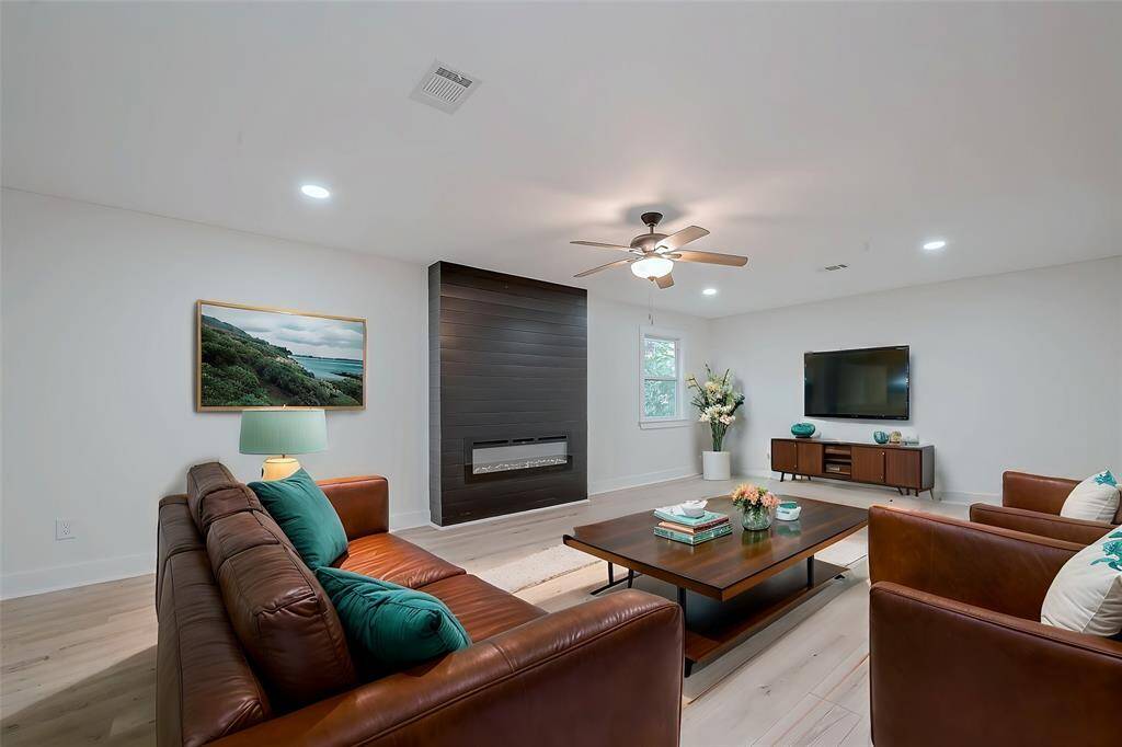Relaxed family room anchored by a sleek black shiplap electric fireplace, warm leather seating, and bright recessed lighting—perfect for cozy gatherings and movie nights.