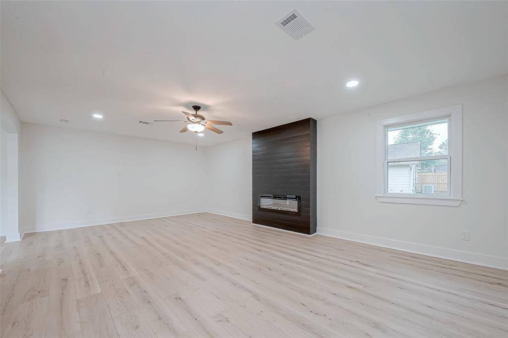 Spacious family room features light-toned wide-plank flooring, recessed LED lighting, and a bold black shiplap fireplace beneath a ceiling fan—an ideal canvas for any décor style.