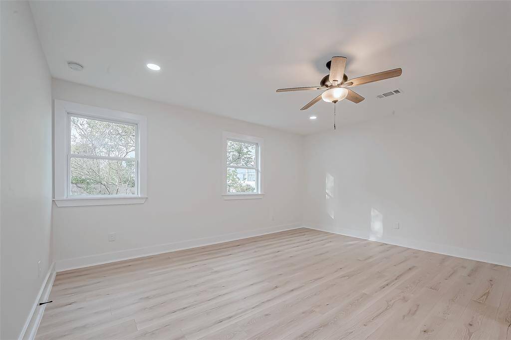 Tranquil secondary bedroom boasts dual windows for abundant natural light, fresh white walls, light wide-plank flooring, and a ceiling fan—ideal for a peaceful night’s rest or a stylish home office.