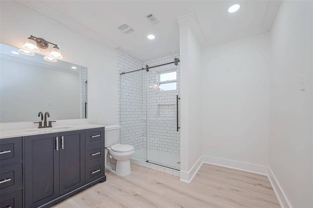 Refined vanity vignette features deep-navy shaker cabinetry topped with quartz, sleek matte-black fixtures, a frameless mirror under a three-light sconce, and subway-tile accents for a polished, spa-like feel.