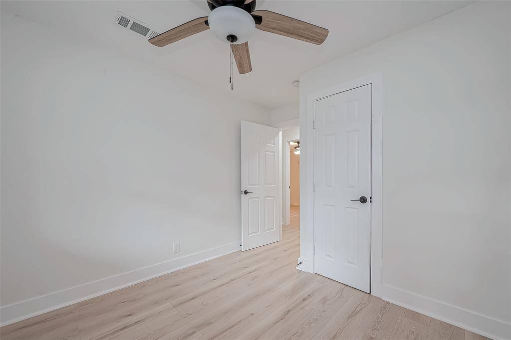 This versatile room features fresh white walls, light-wide plank flooring, matte-black hardware on its built-in closet, and a modern wood-blade ceiling fan—ideal as a guest bedroom, office, or hobby space.
