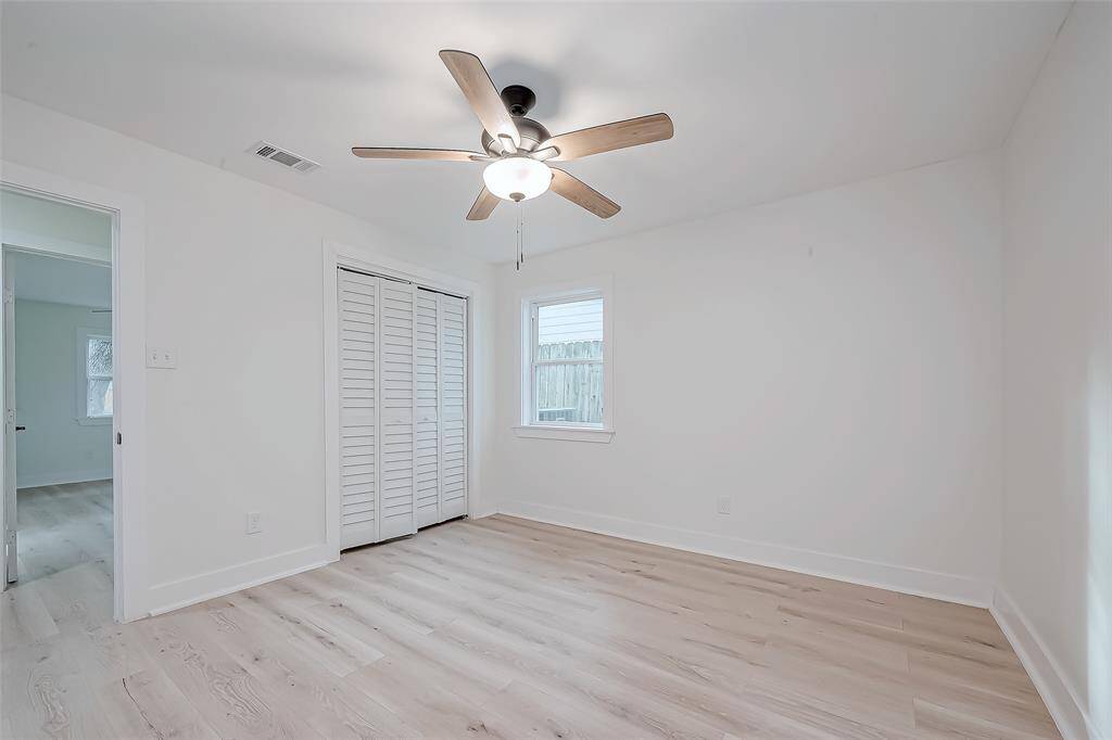 Charming bedroom highlights fresh white walls, light-wide plank floors, louvered closet doors, and a sleek wood-blade ceiling fan—perfect for restful nights or a bright home office.