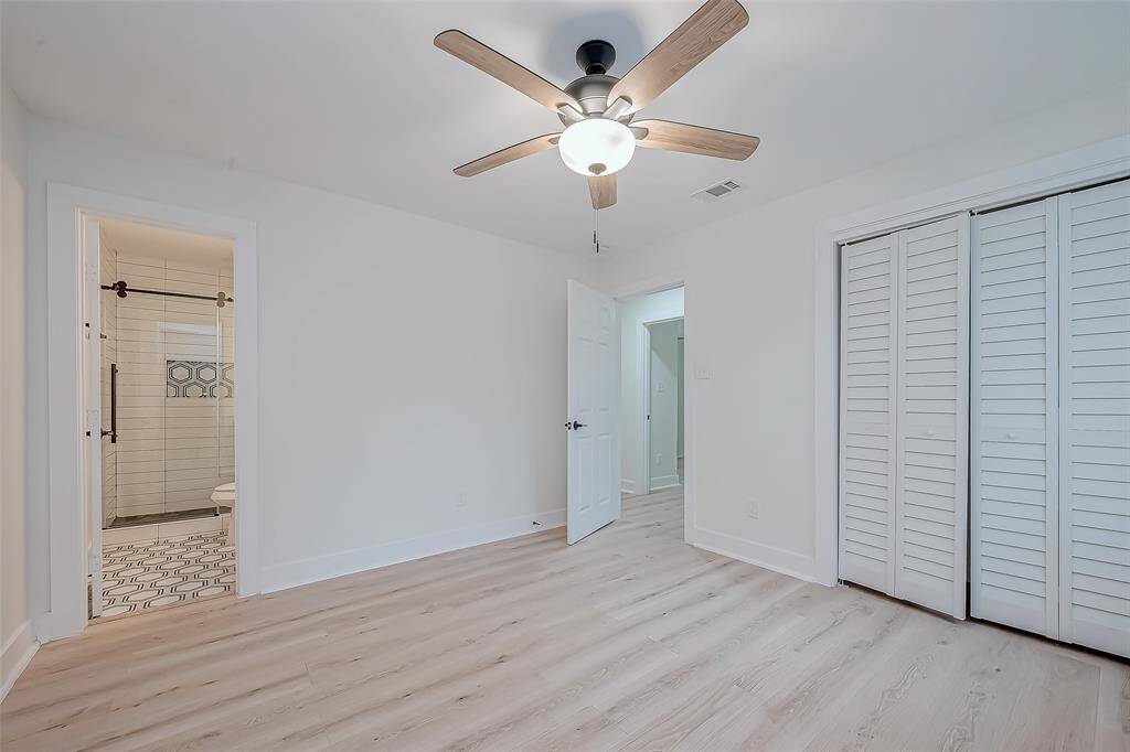 Charming guest suite blends fresh white walls and light-wide plank floors with a louvered closet and modern ceiling fan—plus a boutique-style en-suite featuring patterned tile floors, a subway-tiled walk-in shower with sliding glass door, and matte-black accents for effortless style and privacy.