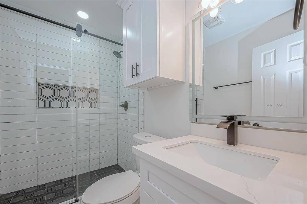 Boutique-inspired en-suite bath showcases a frameless glass shower with elongated subway tile and a striking hex-pattern niche, set off by matte-black fixtures and a sleek quartz-top vanity for a modern, spa-like feel.