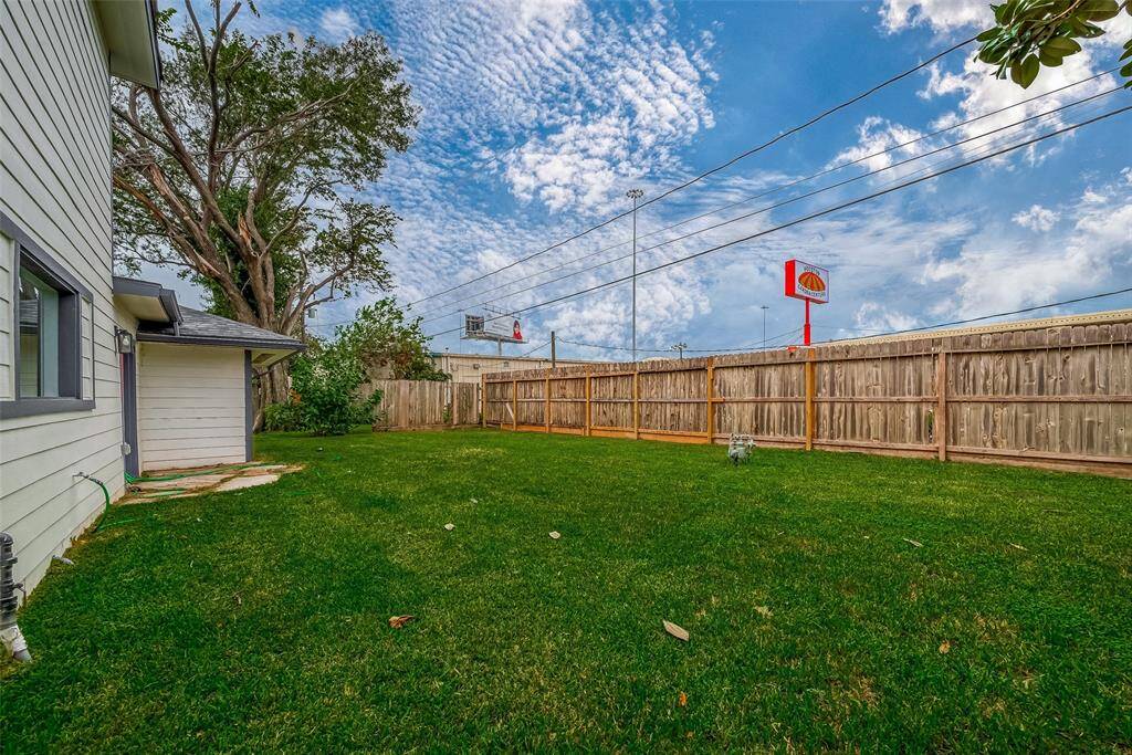 Spacious fenced backyard showcases a lush green lawn framed by a tall wooden privacy fence and a mature shade tree—perfect for outdoor play, gardening, or relaxed alfresco gatherings.
