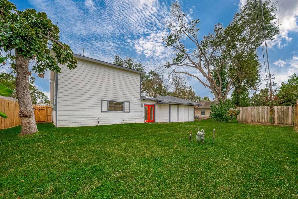 Panoramic backyard vista reveals a generous lawn framed by mature trees and a secure wooden fence, with a vibrant red French door providing a seamless indoor-outdoor connection—ideal for summer barbecues or garden parties.