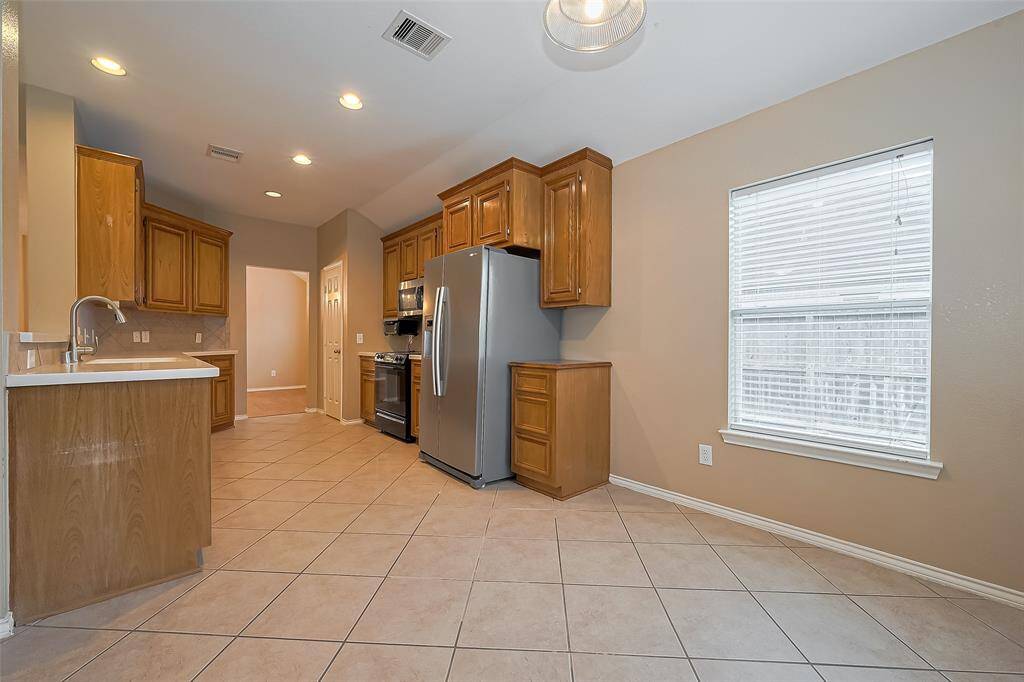 This photo showcases a spacious kitchen with ample natural light, featuring wooden cabinets, a modern stainless steel dishwasher, and a tile backsplash. The open layout connects to an breakfast room, enhancing the home's flow and functionality.