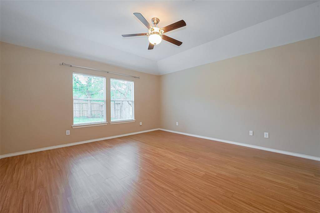 This spacious  primary room features hardwood flooring, neutral walls, a ceiling fan, and two large windows offering plenty of natural light and a view of the backyard.