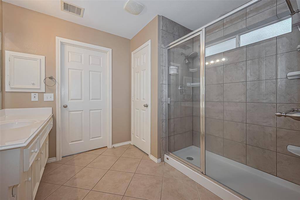 This bathroom features a spacious walk-in shower with glass doors, a large vanity with ample storage, and neutral tile flooring and walls, creating a clean and modern look.