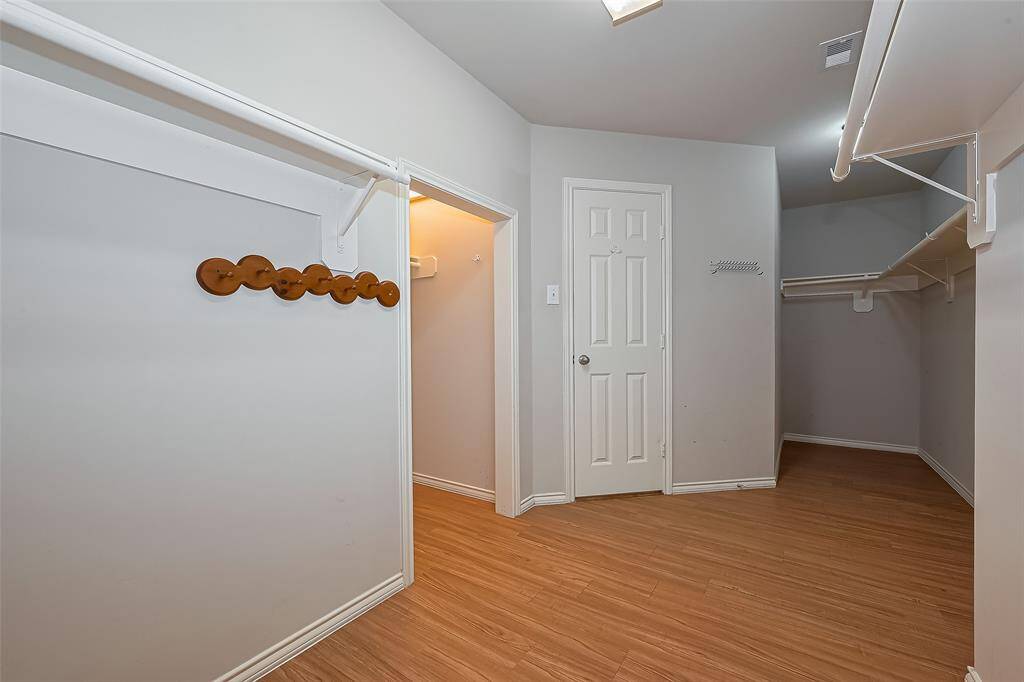 Spacious walk-in closet with wooden flooring, ample hanging space, and a neutral color scheme.