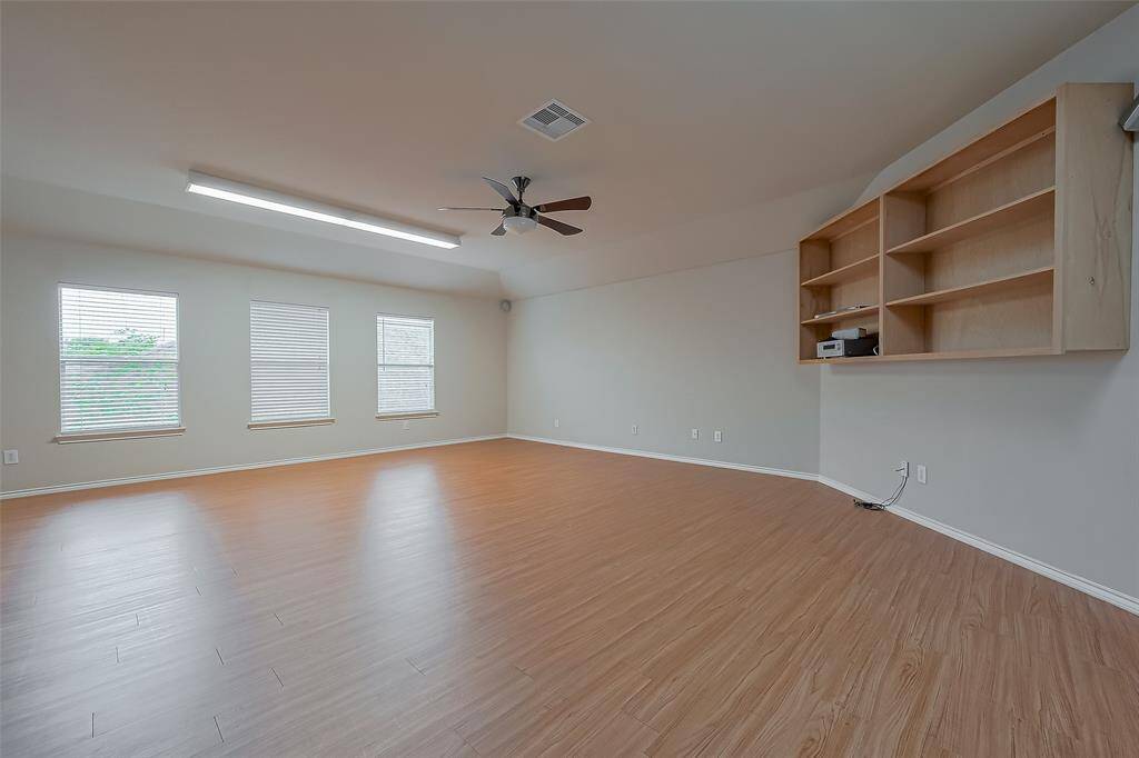Spacious game room upstairs with wood flooring, ample natural light from three windows, a ceiling fan, and built-in shelves, perfect for a home office or entertainment space.