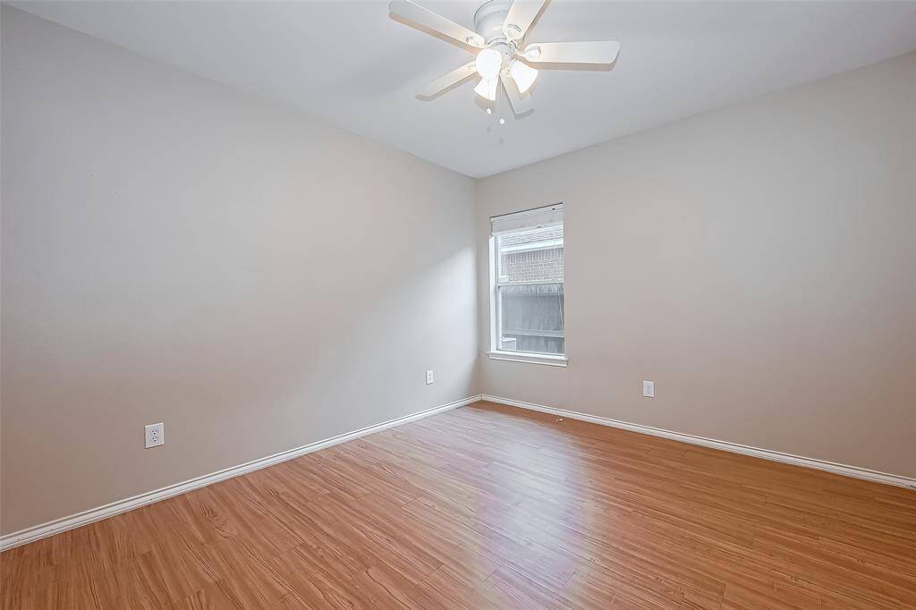 This secondary room features wood-like flooring, a ceiling fan with lights, and a window providing natural light, creating a bright and airy atmosphere.