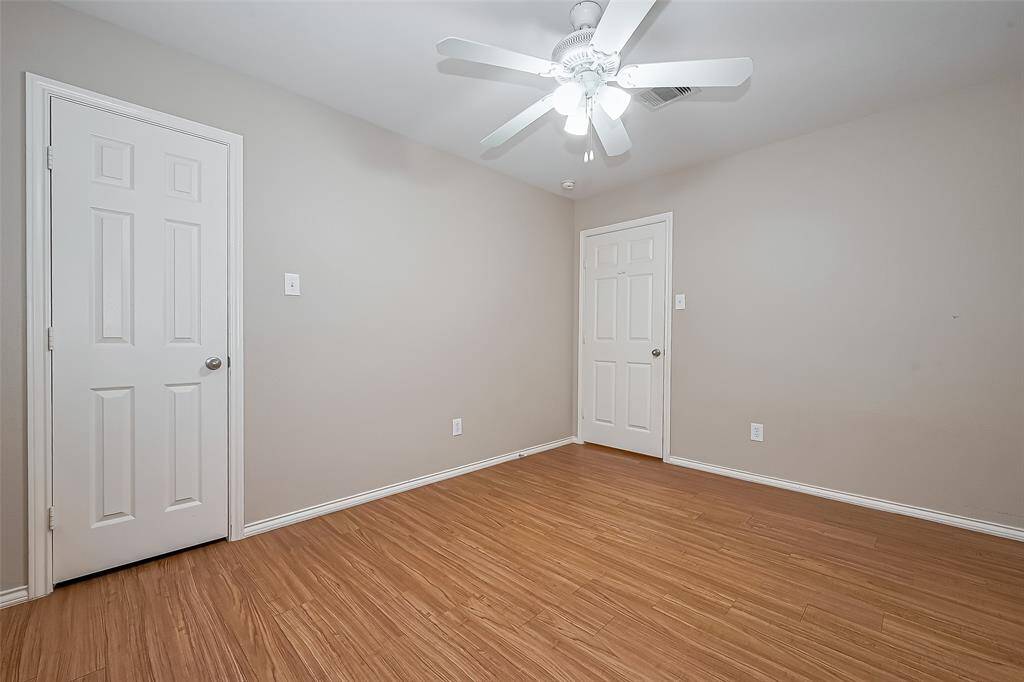 This bright secondary room features neutral walls, wood-style flooring, and a ceiling fan with light. It includes two white doors, providing a clean and versatile space.