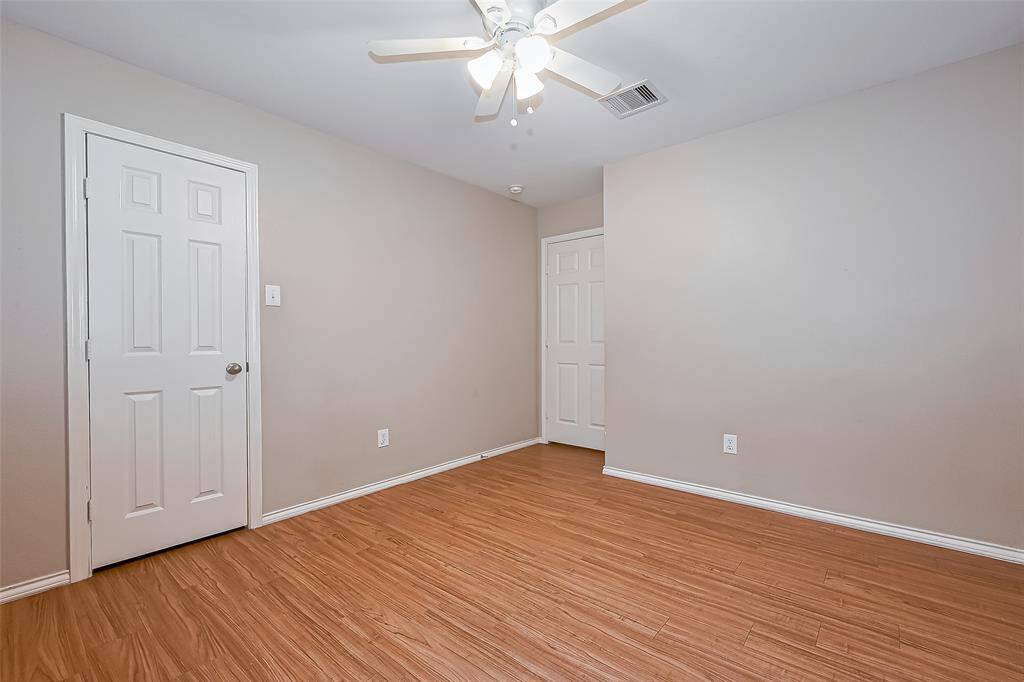 This final secondary room features warm wood flooring, neutral walls, and a ceiling fan, offering a cozy and versatile space. It includes two white doors, providing access and storage options.