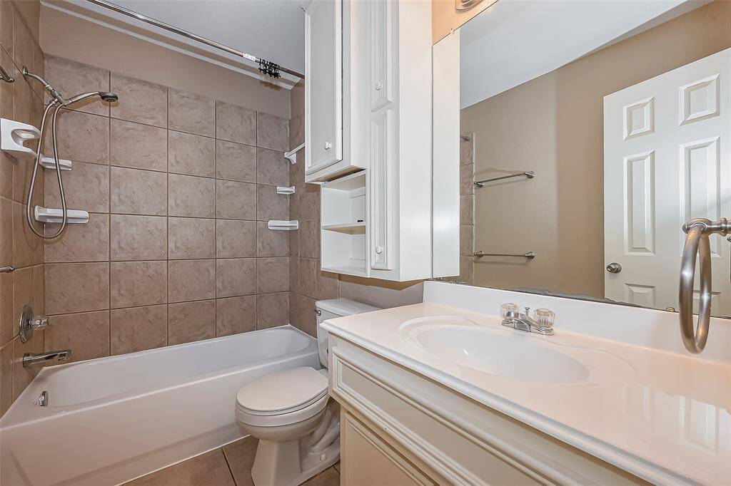 This bathroom features a bathtub with a tile surround, a showerhead, and built-in shelving. It includes a toilet, vanity with sink, and ample cabinet storage. The neutral color scheme provides a clean and inviting look.