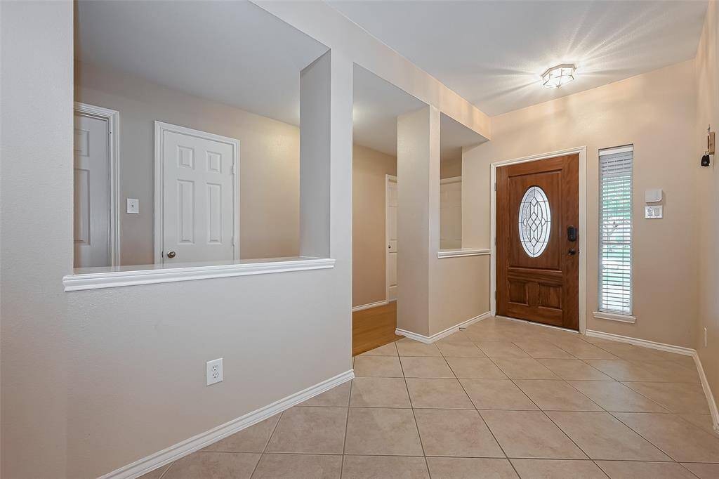 This is a bright, welcoming entryway featuring a stylish wooden front door with an oval glass insert, tile flooring, and neutral wall colors. The space includes a small window and multiple interior doors leading to other areas of the home.