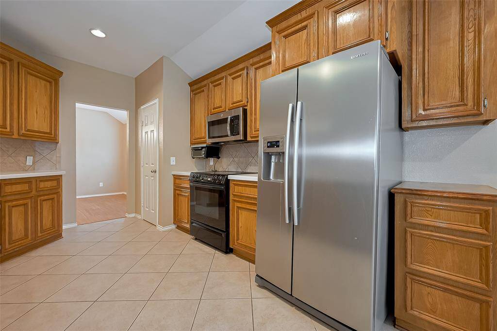 Spacious kitchen with light tile flooring, wood cabinets, and stainless steel appliances. It features ample natural light from a large window and has recessed lighting.
