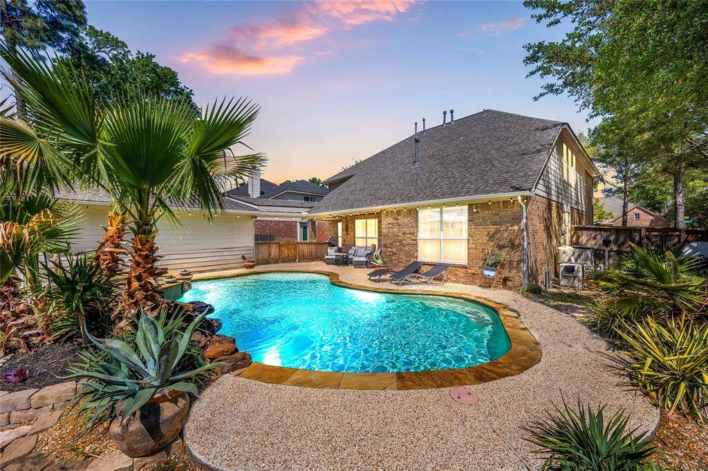 A charming two-story brick home with large windows and a welcoming front entrance. The property features well-maintained landscaping, including trees and shrubs, and a curved walkway leading to the front door.