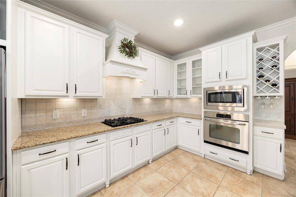 This kitchen features elegant white cabinetry, granite countertops, and stainless-steel appliances, including a built-in oven and microwave. The space is complemented by a tiled backsplash, a wine rack, and a gas cooktop, creating a sophisticated and functional cooking area.