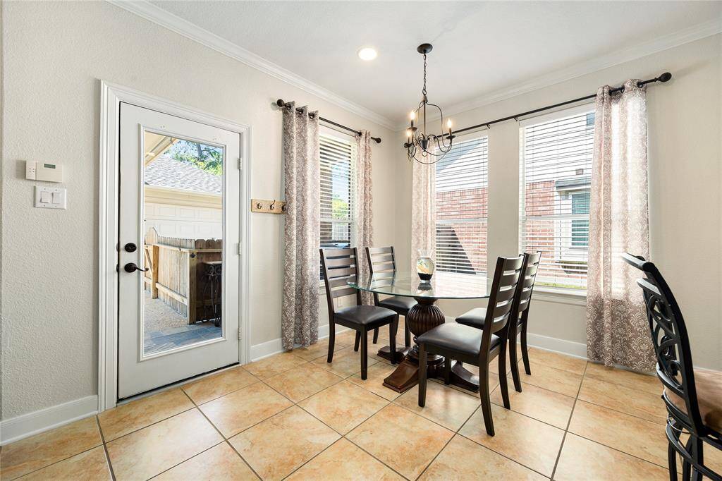 This charming dining area is complemented by large windows that fill the space with natural light. A glass door opens to an outdoor view, framed by stylish curtains and a tasteful chandelier overhead. It’s an ideal setting for intimate gatherings.