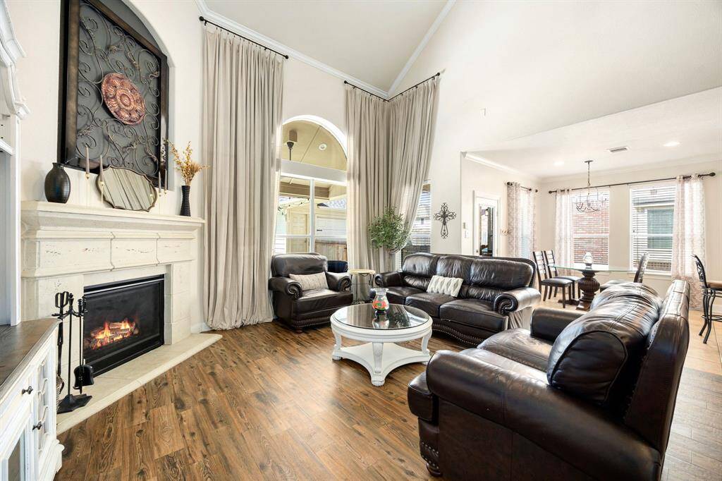 This inviting living space features high ceilings, a cozy fireplace, and elegant wood flooring. Large windows and neutral tones create a bright, airy atmosphere, seamlessly connecting to a dining area perfect for family gatherings.