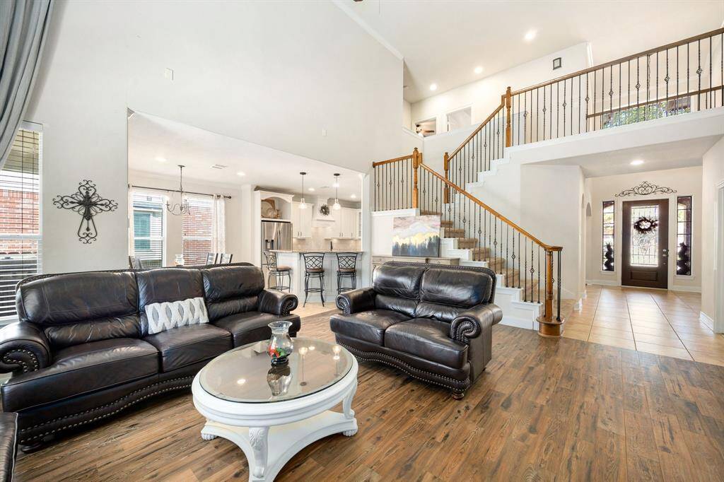 This photo showcases a spacious living room with high ceilings. The open layout connects to a modern kitchen with a breakfast bar. A stylish staircase leads to an upper level, and natural light floods through large windows. The entryway is inviting with a decorative door and tiled flooring.