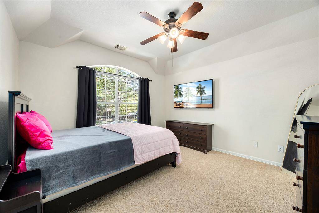This bedroom is bright and inviting, featuring a large arched window with ample natural light. It includes a ceiling fan, neutral carpeting, and a simple layout.