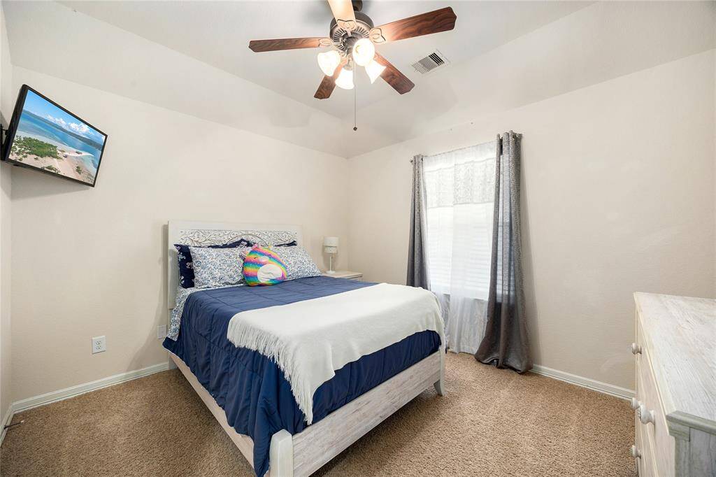 Cozy bedroom with neutral walls and carpet, featuring a ceiling fan and a large window for natural light.