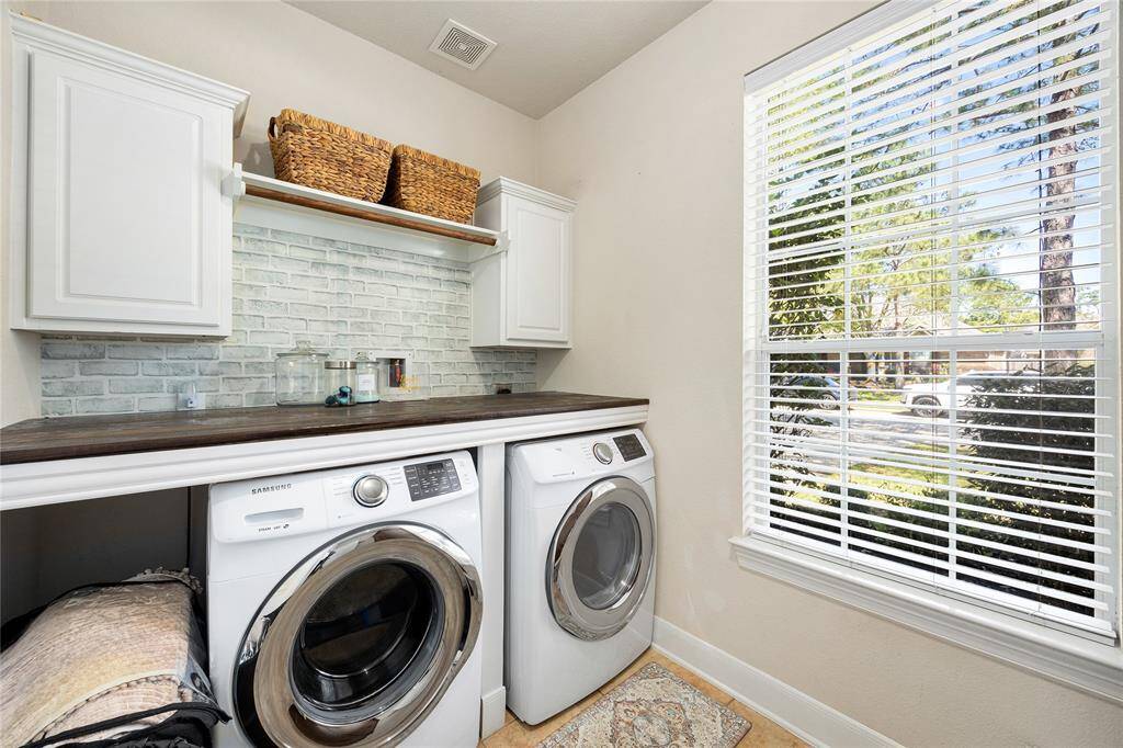 This laundry room features white cabinetry and a stylish brick backsplash. It has a large window for natural light and built-in shelving for storage.