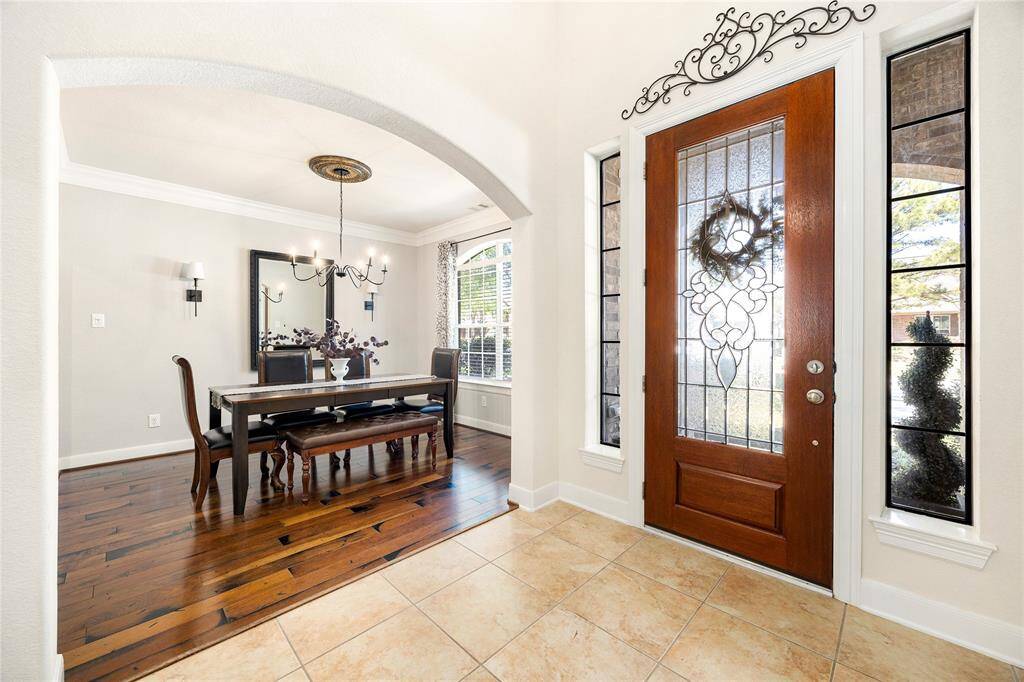This photo showcases a welcoming entryway with a decorative glass front door and sidelights, leading to a dining area featuring elegant wood flooring, a stylish chandelier