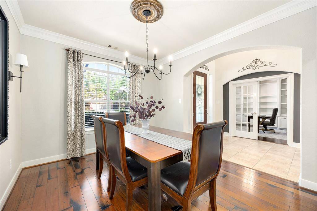 This elegant dining area features hardwood floors, a large window with ample natural light, and a stylish chandelier. It opens to a home office with French doors, creating a seamless flow in the living space.