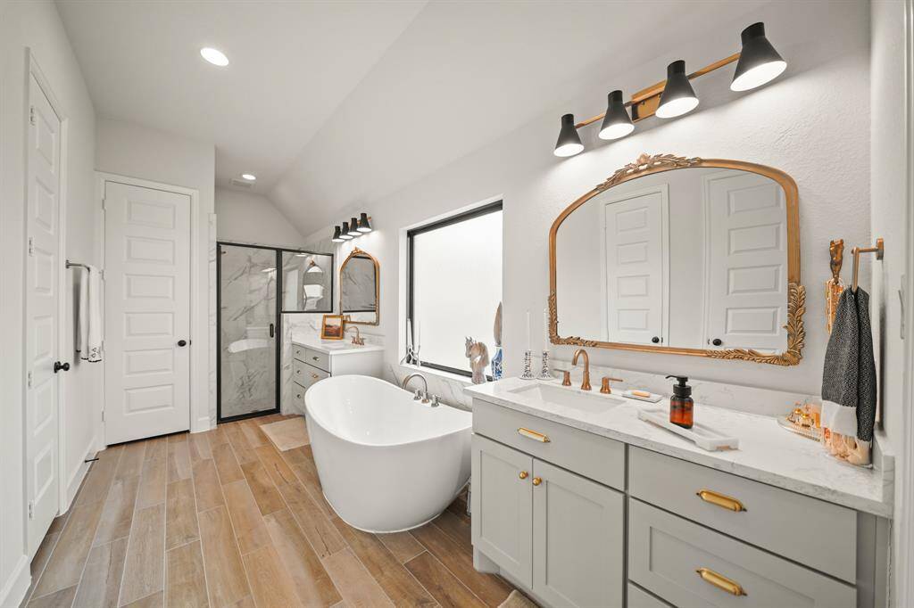 The serene Primary Bathroom blends comfort & elegance with Champagne Bronze finishes, a luxurious freestanding tub, & a pair of graceful Eloise arch mirrors.