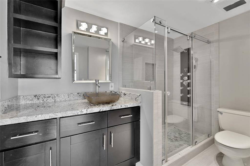 The updated primary bathroom features a walk-in shower with body jets, digital temperature along with a wall shower head and handheld. The vanity includes a bowl sink with counter space and built-in storage above and below.