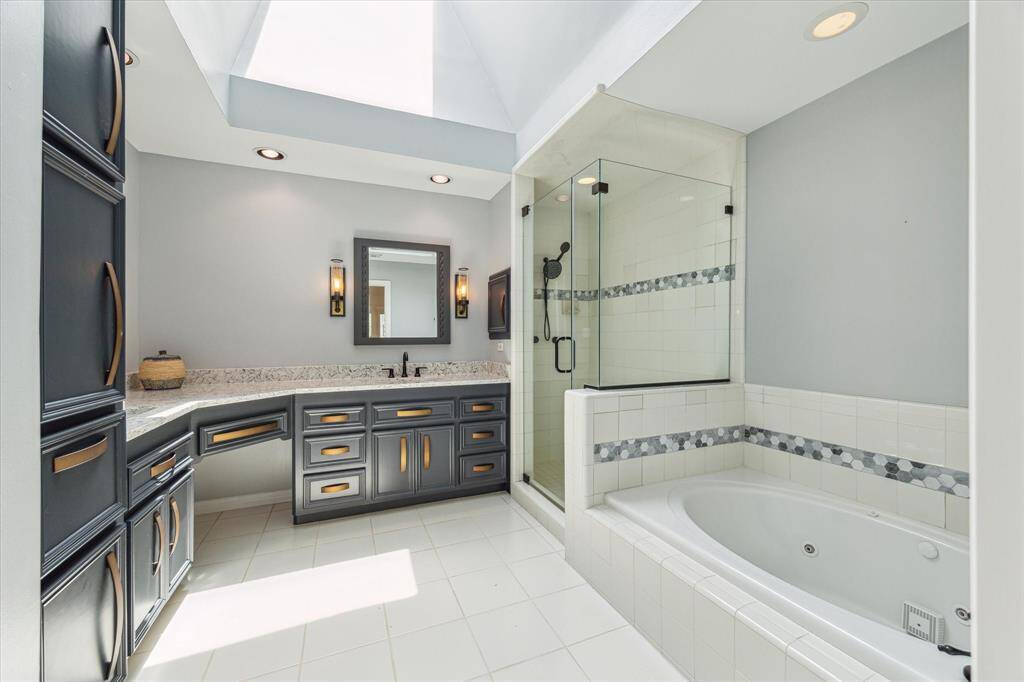 A skylight crowns this luxurious primary bath, where dual vanities with bold cabinetry and sleek hardware frame a spa-inspired soaking tub and walk-in shower.