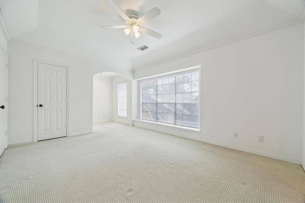 This expansive secondary bedroom features carpet flooring, a ceiling fan with light, crown molding and a large picture window with blinds.
