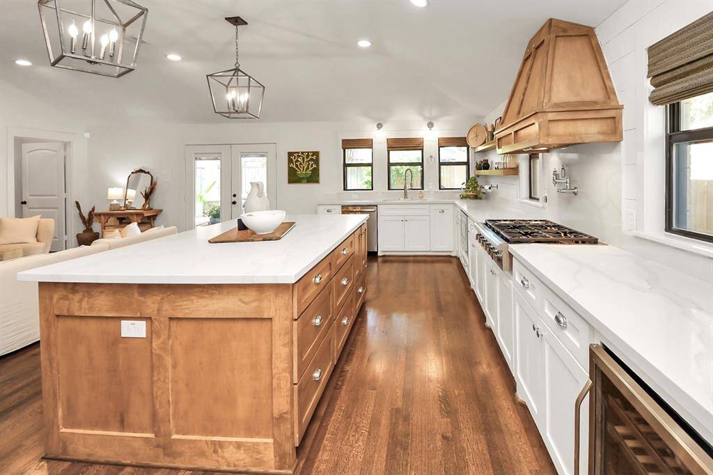 This kitchen features a spacious, bright design with a large central island and wood accents. It includes modern lighting, ample cabinetry, a gas cooktop, and stainless steel appliances. The open layout connects seamlessly to the living area, ideal for entertaining.
