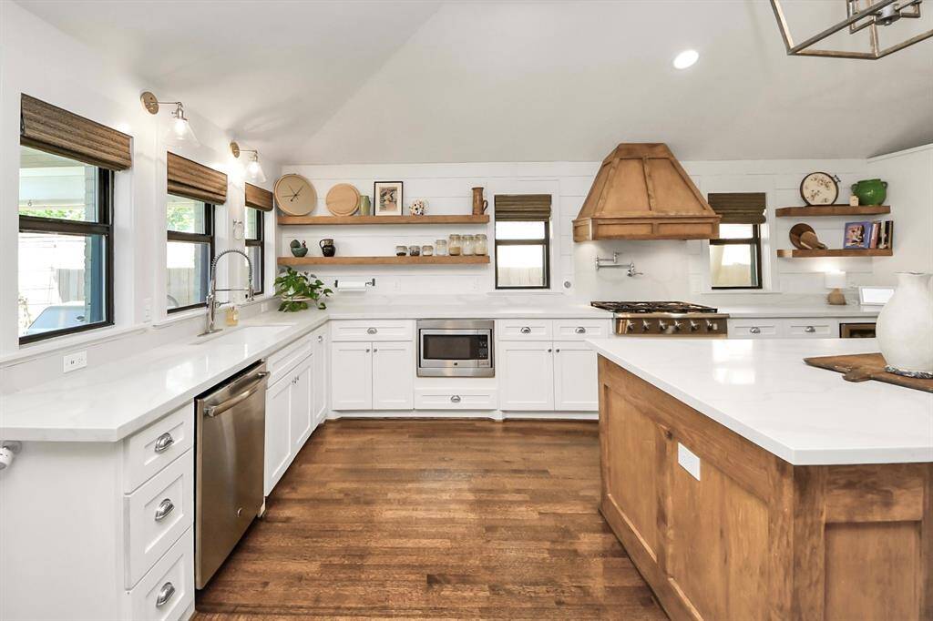This kitchen has a bright, open layout with modern appliances and white cabinetry. Warm wooden accents, a pot filler, and abundant natural light enhance its style and functionality.