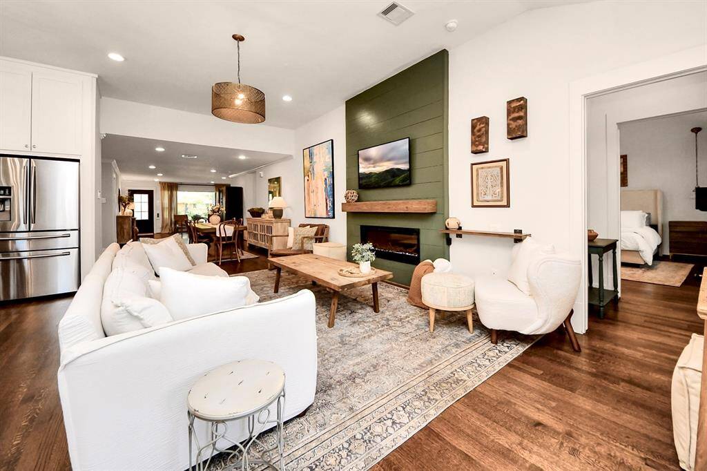 Experience the charm of this bright, open-concept living area featuring hardwood floors and modern accents. Enjoy a cozy seating space around a stylish fireplace, seamlessly flowing into the dining area and a kitchen equipped with stainless steel appliances. A doorway conveniently leads to the bedroom, enhancing the home's inviting and functional layout.
