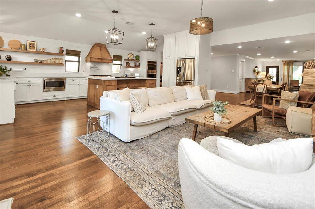 This open-concept living area features a spacious kitchen with modern white cabinetry, wooden accents, and stainless steel appliances. The adjoining living room includes cozy seating, a large sectional sofa, and elegant lighting. The space is bright and inviting, perfect for entertaining or family gatherings.
