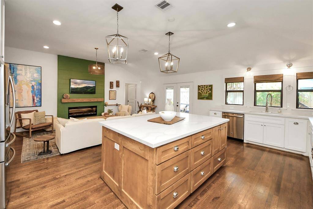 This open-concept living space features a modern kitchen with a large island, stainless steel appliances, and white cabinetry. The adjoining living area includes a cozy fireplace with a green accent wall and ample natural light from multiple windows.