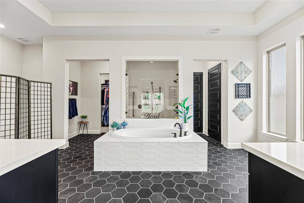 Luxurious primary bathroom featuring a large soaking tub, an oversized walk-in shower with dual shower heads, and striking hexagon tile flooring. Abundant natural light and dual walk-in closets complete this elegant spa-like retreat.