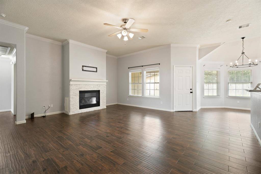 This spacious living area features hardwood floors, a cozy fireplace, and abundant natural light from large windows. The room is enhanced by a ceiling fan and an open layout that flows into a bright dining space.