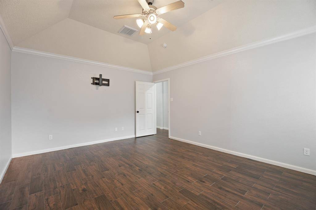 This spacious room features a vaulted ceiling with a ceiling fan, light gray walls, and rich wood flooring, creating a modern and inviting atmosphere.
