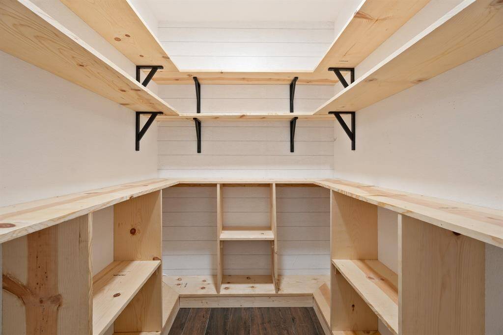 This photo showcases a spacious walk-in primary closet with wooden shelves and a rustic shiplap wall design, ideal for ample storage and organization.