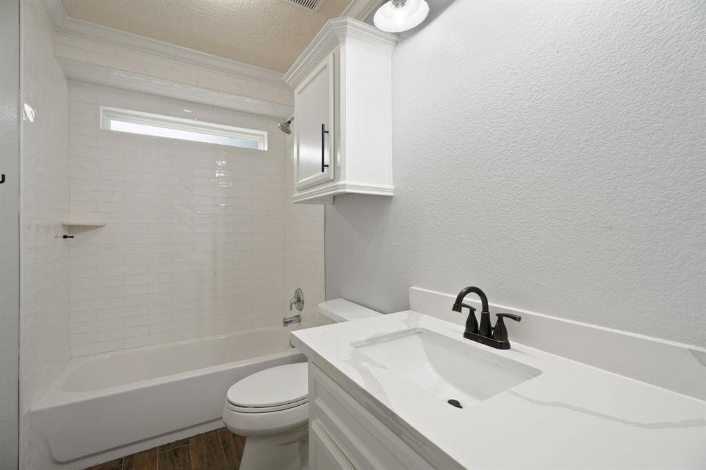 Modern bathroom with white fixtures, featuring a sleek vanity, black faucet, and a tub-shower combo with subway tile. Bright and clean design.